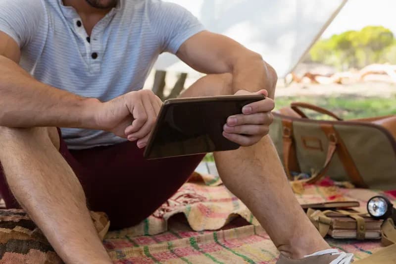 Person sitzt vor einem Zelt und bedient ein Tablet