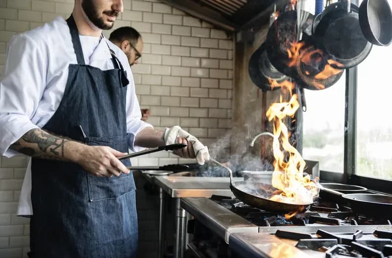 Koch flambiert in einer Pfanne auf einem Gasherd in einer Restaurantküche