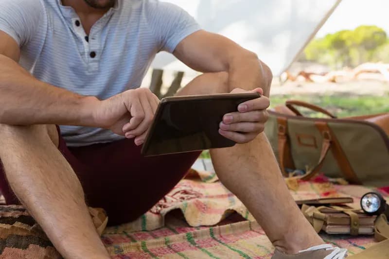 Person sitzt vor einem Zelt und bedient ein Tablet